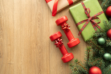 Christmas gift boxes, gym workout dumbbells, tree branches and decorations. Exercise equipment as present idea. Sport gifts flat lay composition with copy space. Healthy fitness winter holiday season.