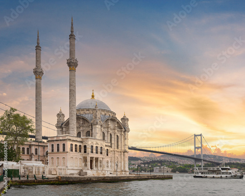 A stunning view of Ortakoy Mosque sitting next to the Bosphorus Bridge with minarets and domes glistening in the rays at sunset in Ortakoy neihborhood, Istanbul, Turkey photo