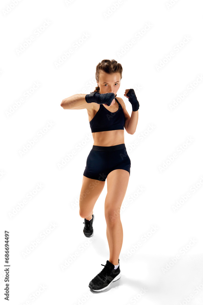 Dynamic full length portrait of sportsman, female boxer, exuding strength and confidence, against clean white studio background. Dynamic full length portrait of sportsman, female boxer, exuding strength and confidence, against clean white studio background.