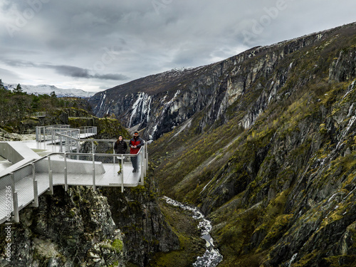 Obraz na płótnie A couple stands on the edge of the observation platform above Vøringfossen waterfall with the canyon in the background, drone photo w salonie
