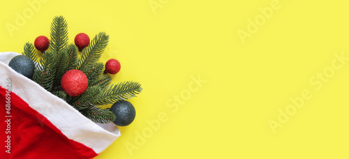 Fototapeta Naklejka Na Ścianę i Meble -  Fir branch with Christmas balls in a Santa Claus hat on a yellow background, top view. New Year banner with empty space. Copy space. New Year's branch with decor