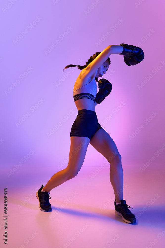 Portrait of focused female boxer, her body testament to her dedication, poses powerful against gradient studio background in neon light.