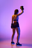 Rear view portrait of athletic female sportsman, professional boxer in sportwear rejoicing victory against gradient background in neon light.