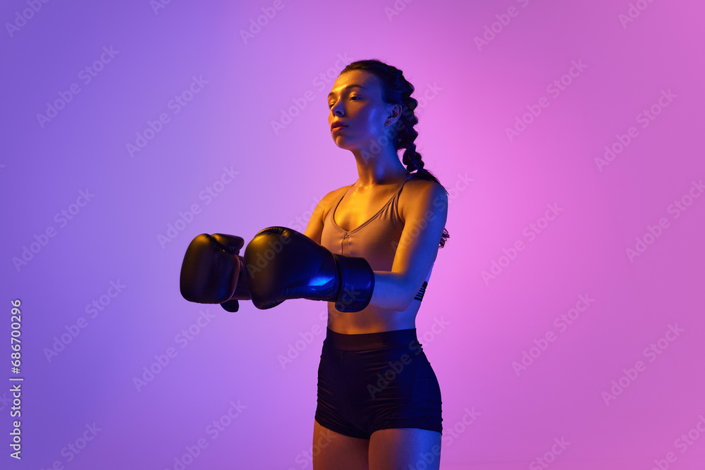 Intense and captivating, a professional boxer girl stands out against gradient pink-violet studio background in neon light.