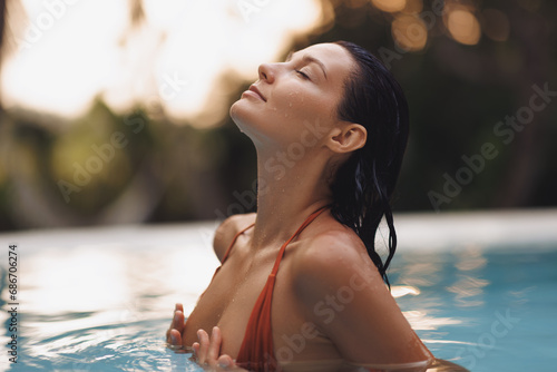 Tropical paradise, luxury relaxation of bikini brunette woman in sexy orange swimsuit in infinity pool at sunset covering her breast by hands. High quality portrait photo photo
