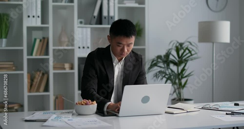 Young asian businessman noting new ideas, eating cereals and typing keyboard. 