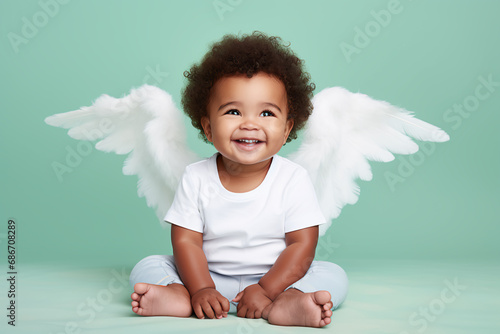 A smiling african american baby, resembling an angel, sits on the floor with white wings, radiating pure happiness,pastel green background.