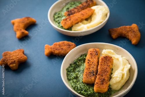 Gebratene Fischstäbchen und Figuren als Fisch, Seestern und Delfin für Kinder mit Rahmspinat und Kartoffel Püree in Schale mit dunkel blau Hintergrund