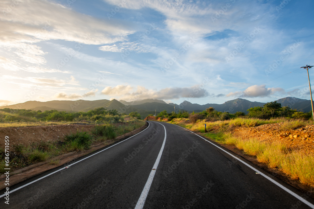 Fototapeta premium Sunrise in the desert. Tour of a desert island, full of xeric vegetation. Cactus and red earth. Mountains, clouds and sun
