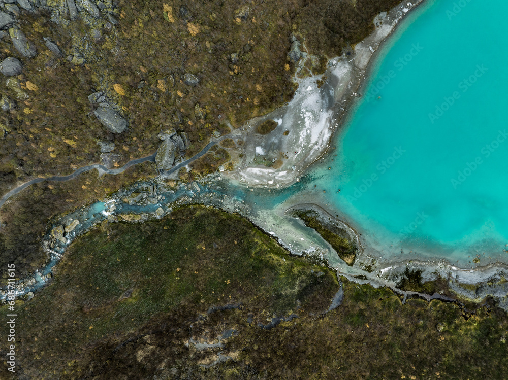 An aerial view of the blue water of the mountain lake of the Briksdalsbreen Glacier transforming into a river