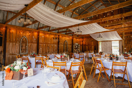 A wedding barn venue with decorated tables, fairy lights and draping chiffon hanging on top.
