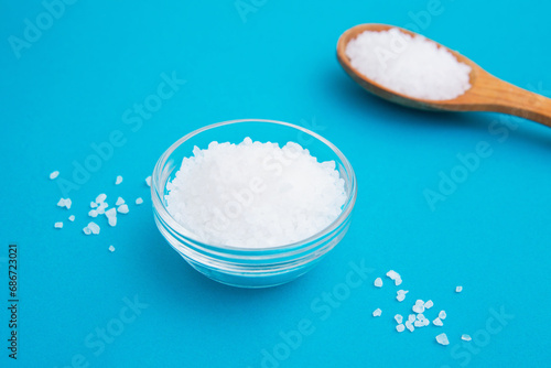 Wooden spoon with salt and glass bowl on the bright blue background