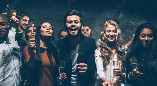 Group of happy young friends holding champagne flutes and sparklers while having fun in night club together
