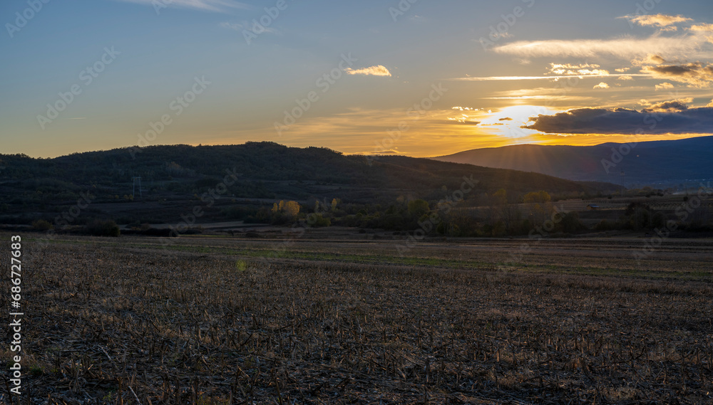 Sunset over the mountain. The sun's rays fall on the plowed fields and on the forest at the bottom of the mountain. Sunset over the mountain. The sun's rays fall on the plowed fields and on the forest at the bottom of the mountain.