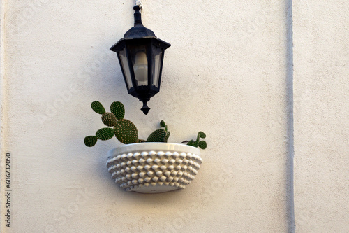 View of a light colored wall with a decorative lantern and small flower pot with a small cute cactus. Typical decoration of walls of residential building in Sicily. Santo Stefano di Camastra village photo