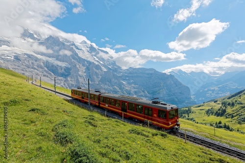 A tourist cogwheel train travels from Jungfraujoch to Kleine Schydegg on the green grassy hillside with top of Jungfrau Mountain covered by clouds, in Berner Oberland (Bernese Highlands), Switzerland