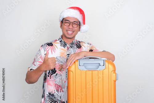 A man with luggage wearing christmas hat smiling and give thumb up photo