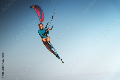 Caucasian woman kitesurfer athlete doing a trick in the air against a blue sky without a cloud. Professional kitesurfing training
