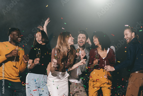 Group of smiling young people enjoying party in the night club with confetti flying around