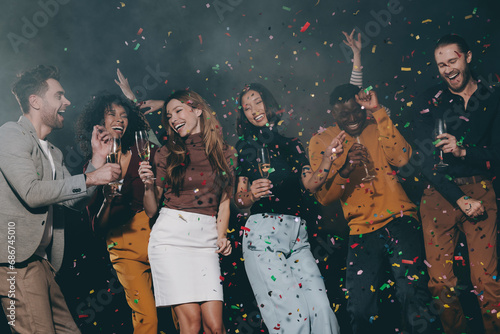 Group of smiling young people enjoying New Year party in the night club with confetti flying around