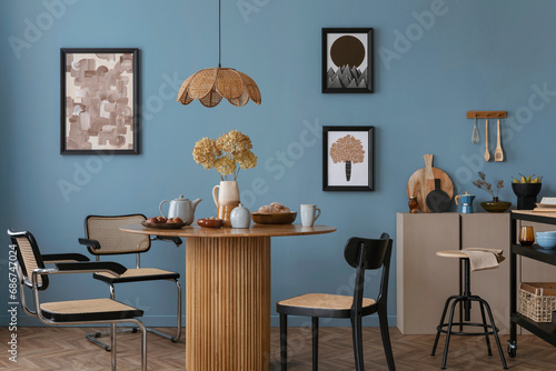 Interior design of warm dinning room interior with mock up poster frame, round table, rattan chairs, beige sideboard, stylish lamp, blue wall and personal kitchen accessories. Home decor. Template.