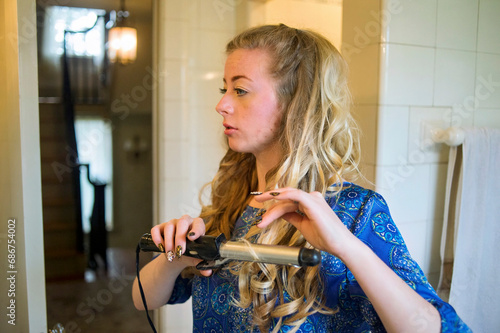 Teenage girl curls her long blond hair as she gets ready for her senior prom; Lincoln, Nebraska, United States of America photo