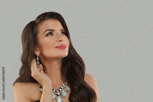 Gorgeous jewelry woman brunette fashion model with gold diamond earning and luxury necklace posing against gray studio wall banner background