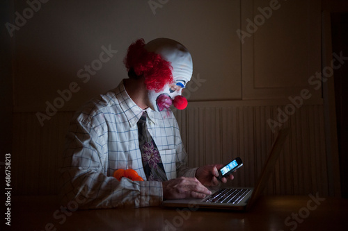 Clown wearing a shirt and tie uses a laptop computer and smart phone simultaneously; Lincoln, Nebraska, United States of America photo