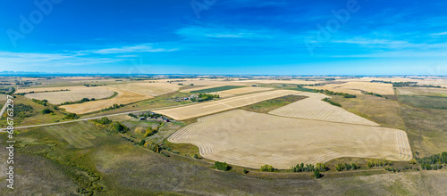 Panorama aerial view of a patchwork of golden grain fields with wispy clouds and blue sky, Southwest of Calgary, Alberta; Alberta, Canada