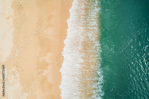 Aerial view of sandy beach and turquoise ocean. Top view of ocean waves reaching shore on sunny day. © Евгений Бахчев