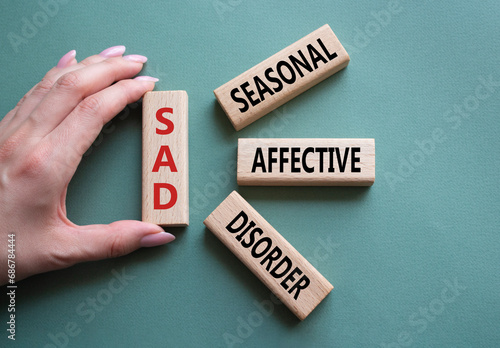 Sad - Seasonal Affective Disorder symbol. Wooden blocks with words Sad. Businessman hand. Beautiful grey green background. Business and Sad concept. Copy space.