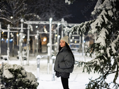 Fototapeta Naklejka Na Ścianę i Meble -  Young woman walking on walkway among snowy winter park at night.
