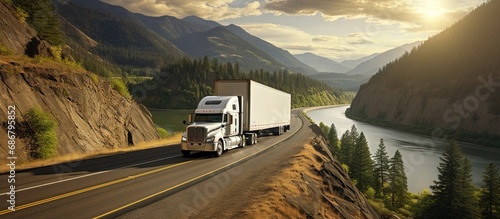 Large white semi truck carrying cargo in a trailer driving on a winding highway with a fence and forest in Columbia Gorge Copy space image Place for adding text or design photo