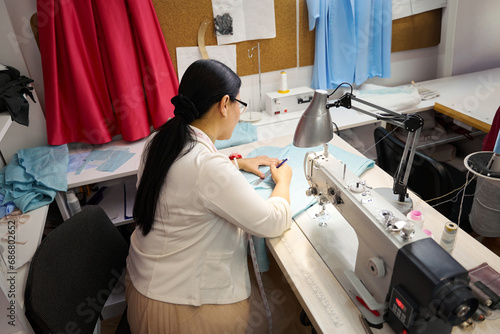 Dressmaker at workplace works with blue fabric
