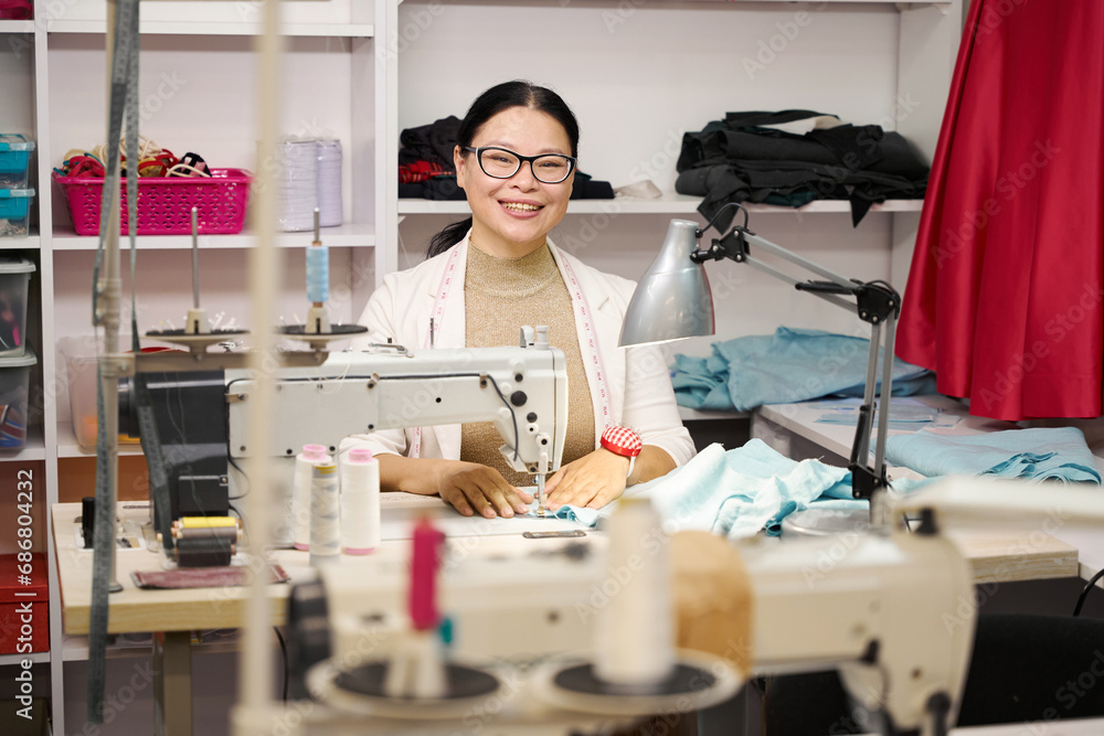 Obraz premium Smiling dressmaker sews on a sewing machine