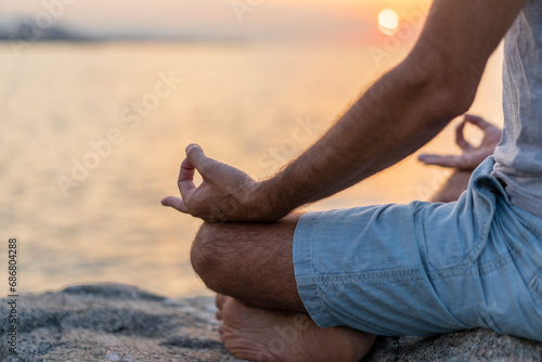 Spain. Man meditating during sunrise on rocky beach, mudra