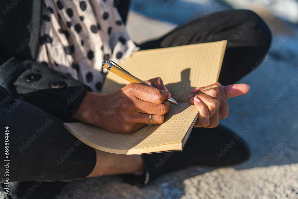 Woman sitting on a wall writing in notebook, close-up