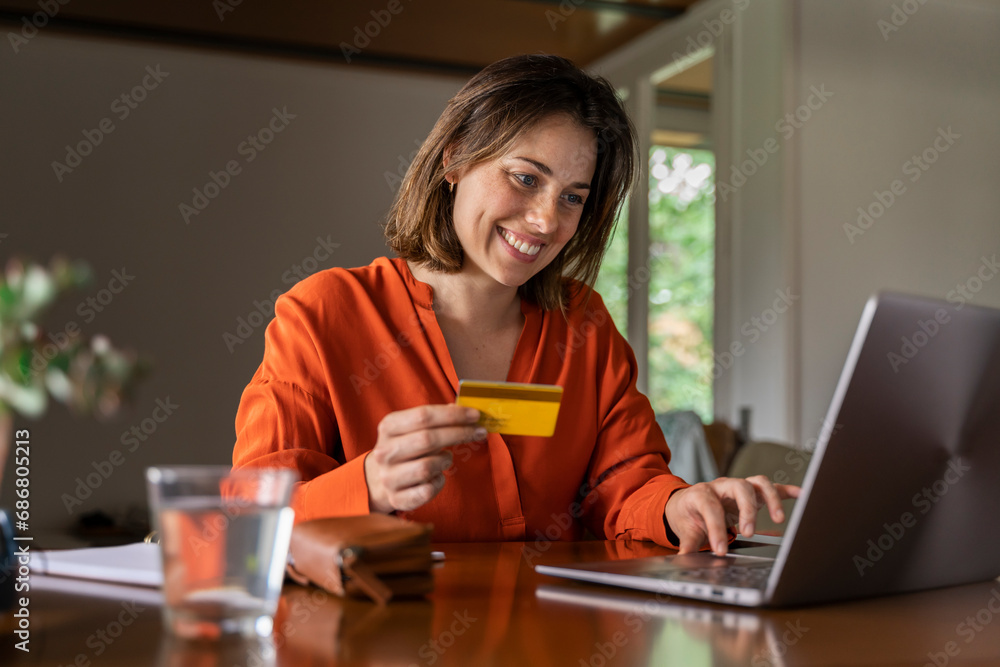 Smiling businesswoman with credit card using laptop at home Smiling businesswoman with credit card using laptop at home