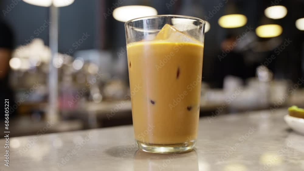 Inviting scene in a cafe with a refreshing ice coffee elegantly presented. The beverage skilled barista walks in the background, element of energy and craftsmanship laid back coffee shop ambiance. Inviting scene in a cafe with a refreshing ice coffee elegantly presented. The beverage skilled barista walks in the background, element of energy and craftsmanship laid back coffee shop ambiance.