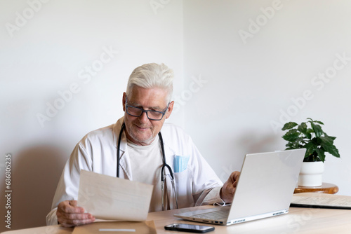Smiling doctor looking at medical record while sitting against wall photo