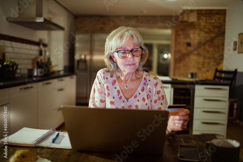 Senior woman looking at credit card at home with laptop photo