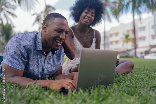 USA, Florida, Miami Beach, laughing young couple looking at laptop on lawn in a park photo