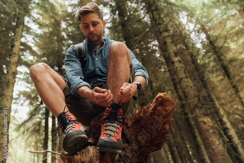 Mid adult man tying shoelace while sitting on wood against trees in forest