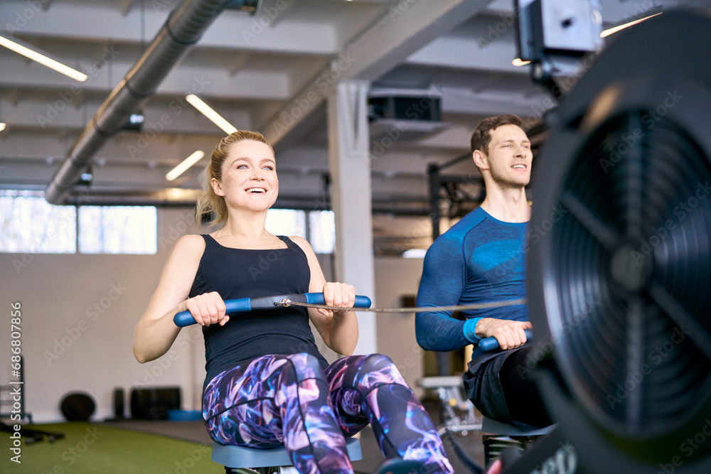 Obraz premium Man and woman at gym exercising together on rowing machines