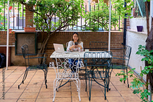 student in the courtyard of his house using his smartphone during a break from studying on the computer.