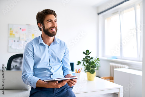 Smiling businessman with headphones using a digital tablet in his office