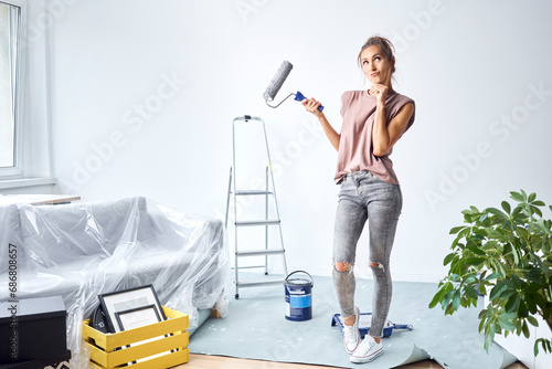Fototapeta Naklejka Na Ścianę i Meble -  Thoughtful woman with head in hands holding paint roller while standing at home