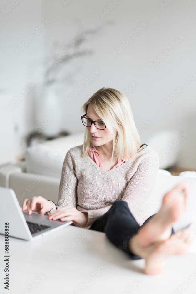 Blond woman sitting at table with feet up using laptop Blond woman sitting at table with feet up using laptop