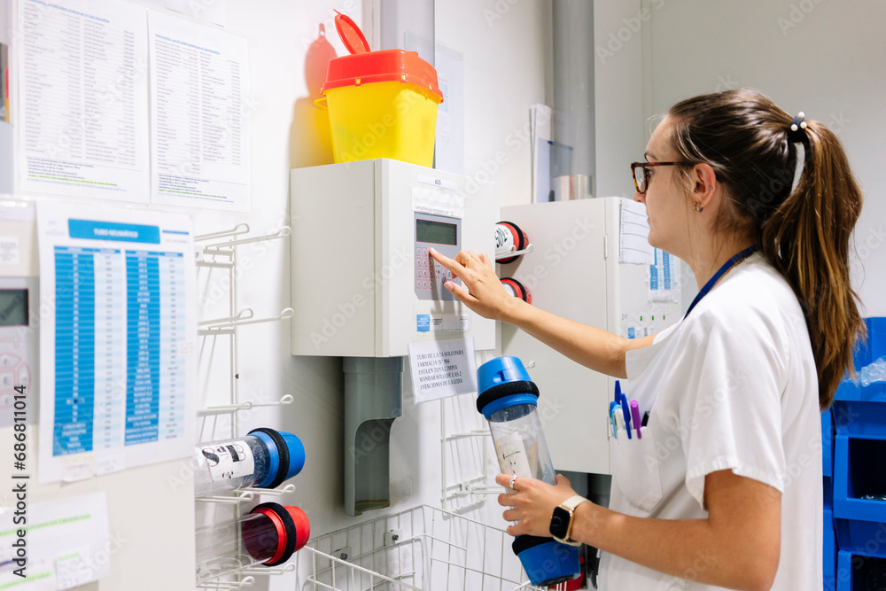 Female doctor using pneumatic tube system while standing in hospital