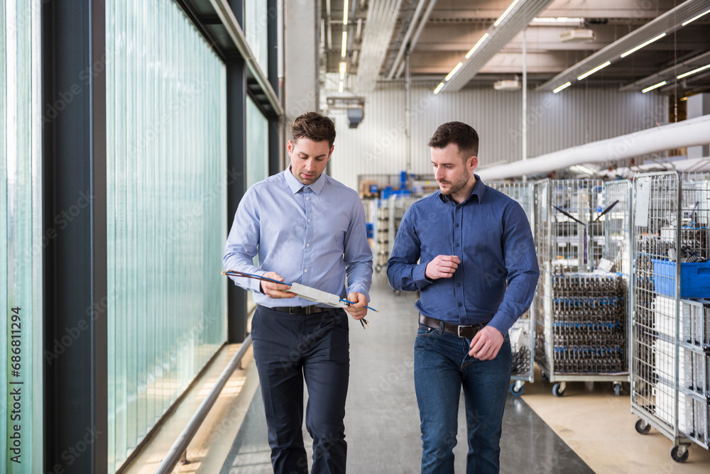 Two men walking in factory shop floor talking about product Two men walking in factory shop floor talking about product